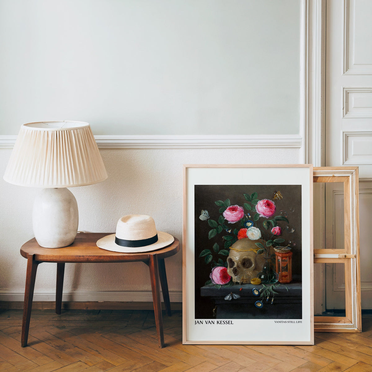 Dark floral still life poster in a light wood frame leaning by a bench and hat