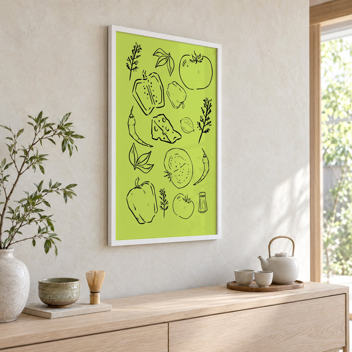 Veggie and cheese line art on green print in a white frame above a pale wood console with a matcha tea set