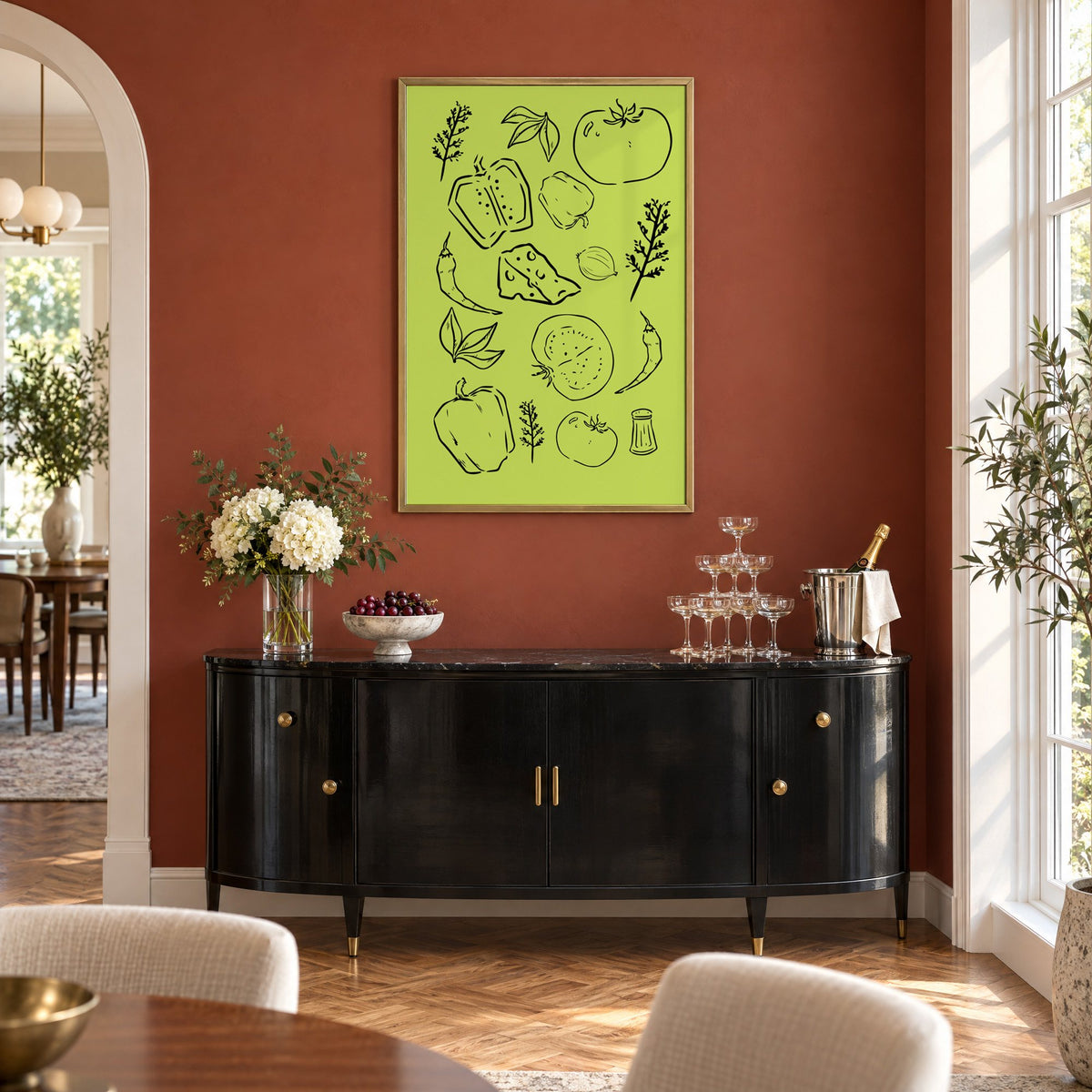 Veggie and cheese line art on green print in a brass frame on a terracotta wall above a black buffet with a champagne tower