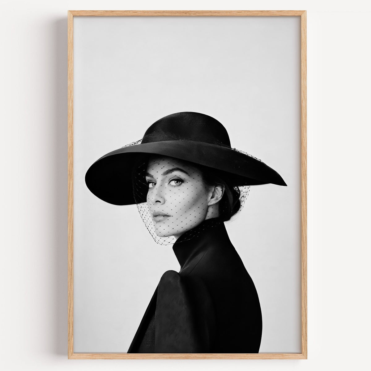 Woman in wide brim hat and mesh veil print in a light oak frame on a plain white wall