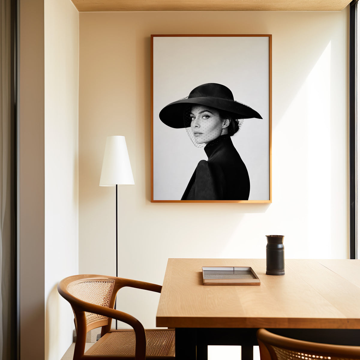 Woman in wide brim hat and mesh veil print in an oak frame above a dining table and cane chair