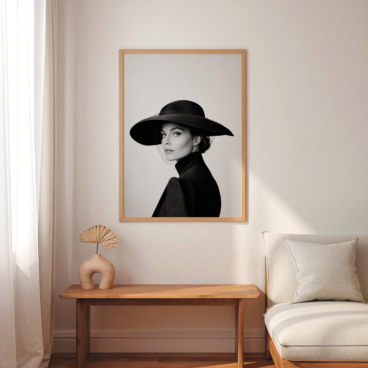 Woman in wide brim hat and mesh veil print in an oak frame above a narrow console with an arched vase