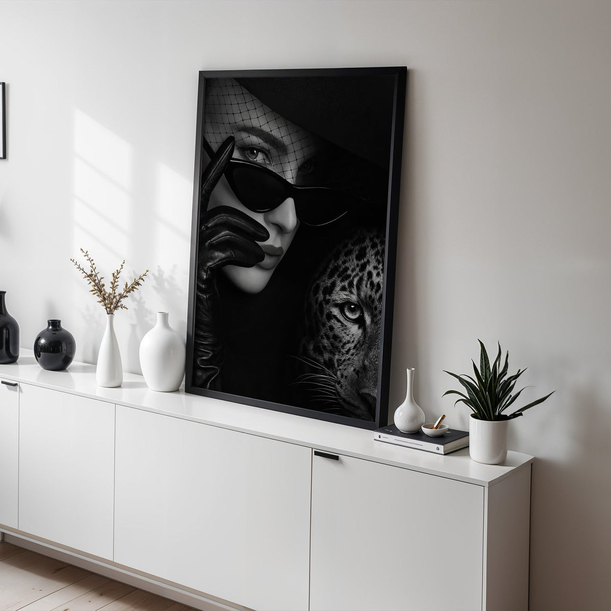 Veiled woman in cat eye glasses with leopard print in a black frame on a white sideboard with black and white vases