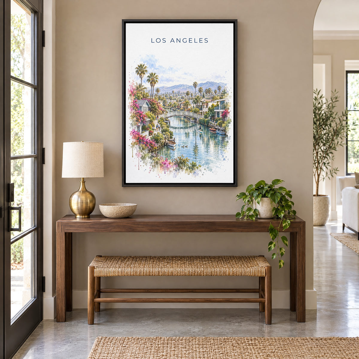 Venice Canals Los Angeles watercolor print as a black floater canvas above a walnut console and woven bench in an entryway