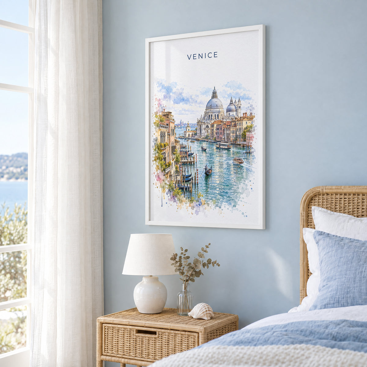 Venice watercolor print in a white frame on a pale blue wall beside a rattan bed in a coastal bedroom