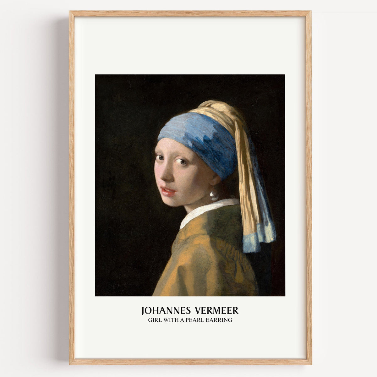 Vermeer Girl with a Pearl Earring print in a light oak frame on a plain white wall