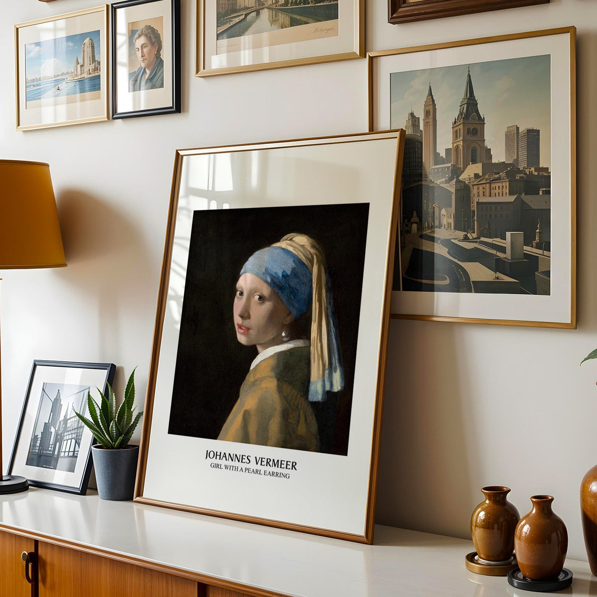Vermeer print shown in a gold frame leaning on a sideboard in a gallery wall