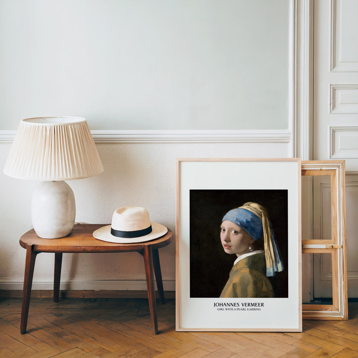 Vermeer poster in a light wood frame leaning by a bench and panama hat