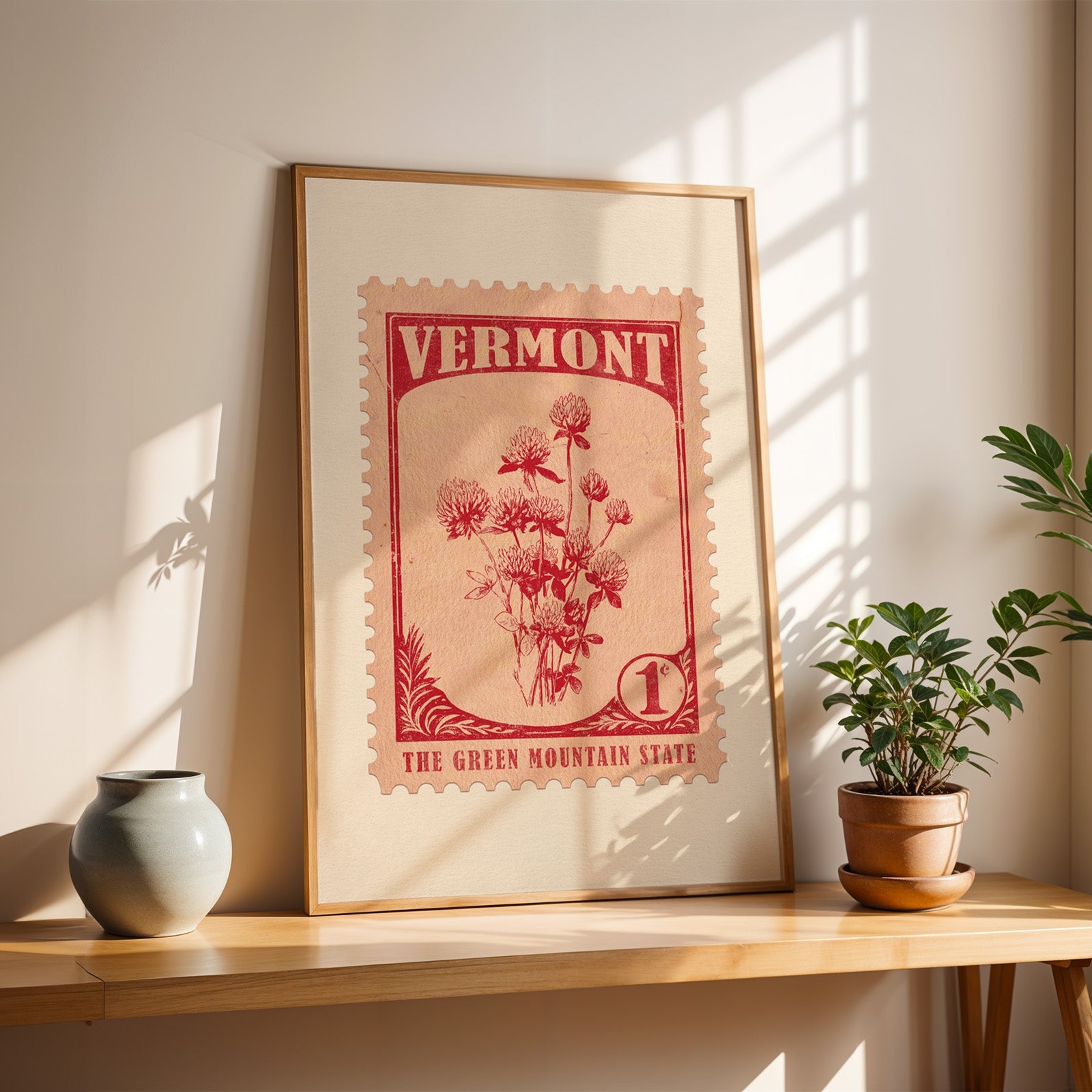 Vermont Red Clover stamp print in a light oak frame leaning on a wooden table beside a stoneware vase