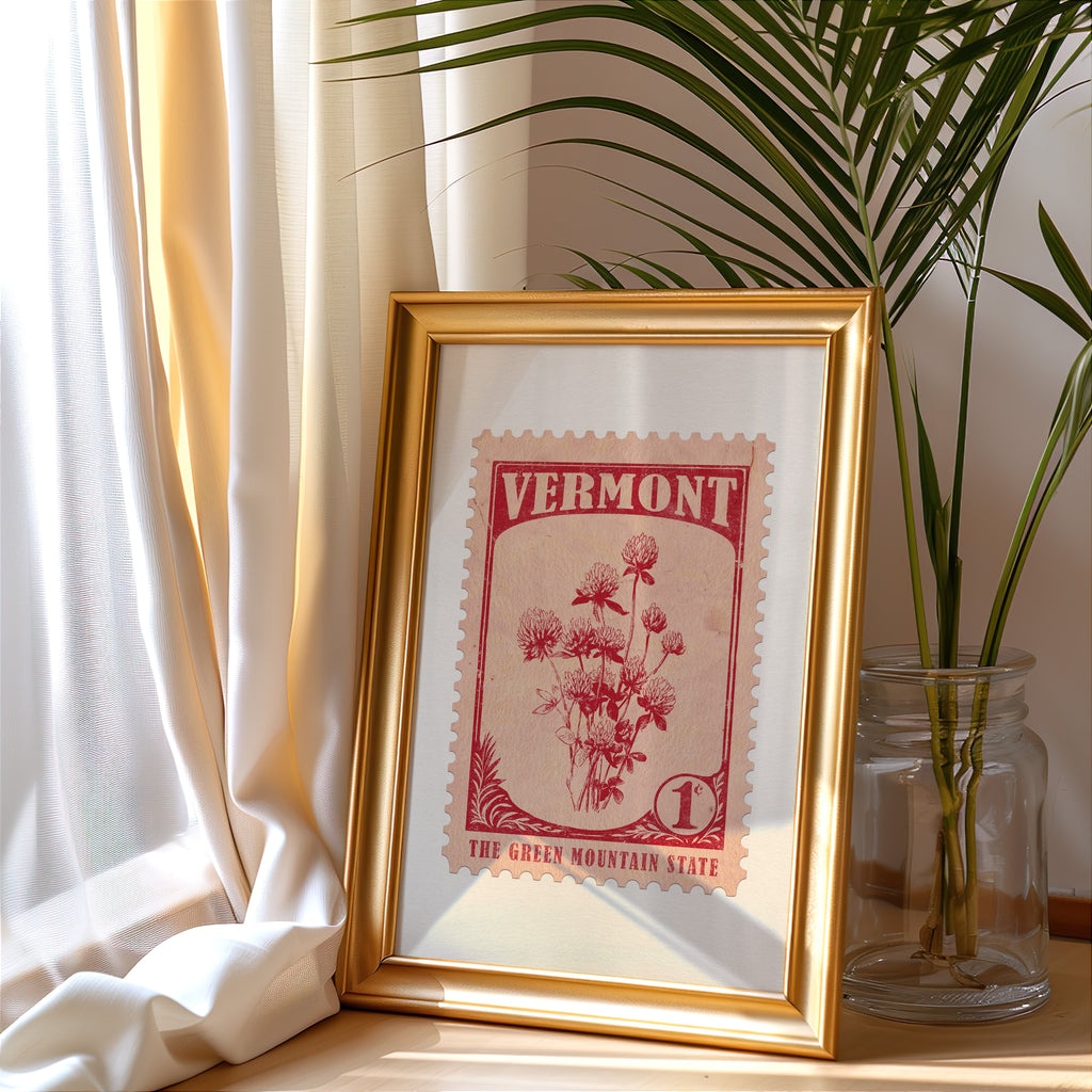 Vermont stamp print in a gold frame leaning by a cream curtain with a palm in a glass jar