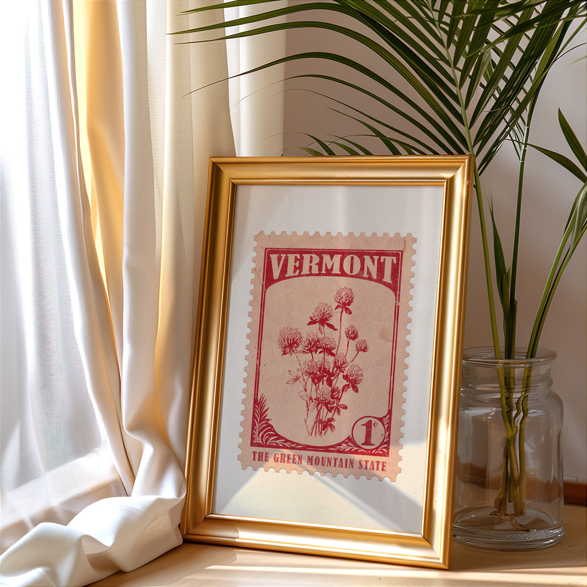 Vermont stamp print in a gold frame leaning by a cream curtain with a palm in a glass jar