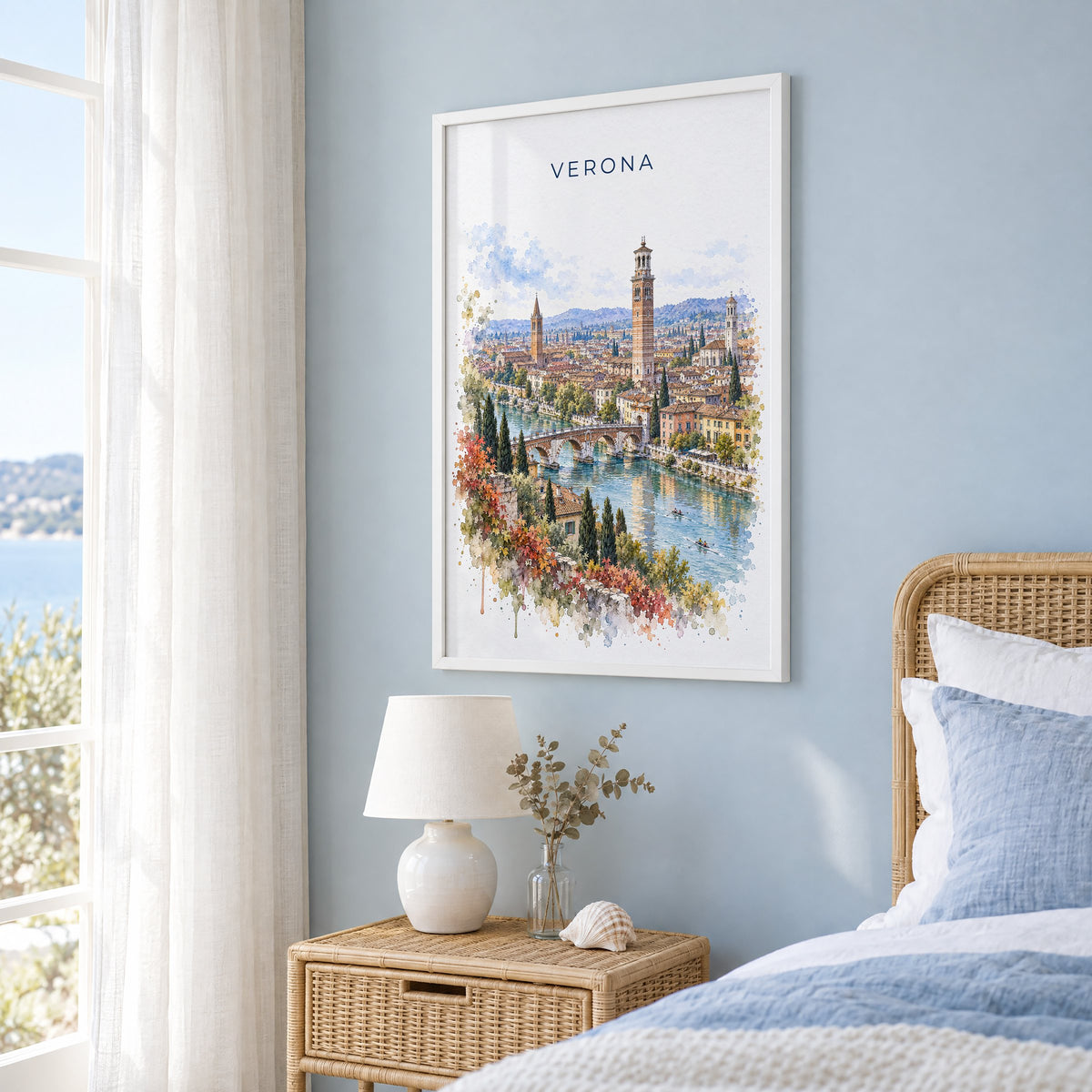Verona watercolor print in a white frame on a pale blue wall beside a rattan bed in a coastal bedroom
