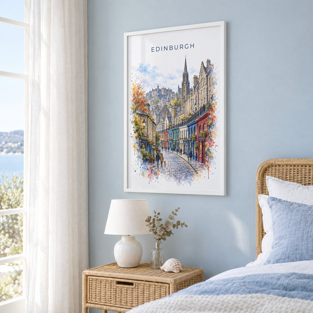 Victoria Street Edinburgh watercolor print in a white frame on a pale blue wall beside a rattan bed in a coastal bedroom