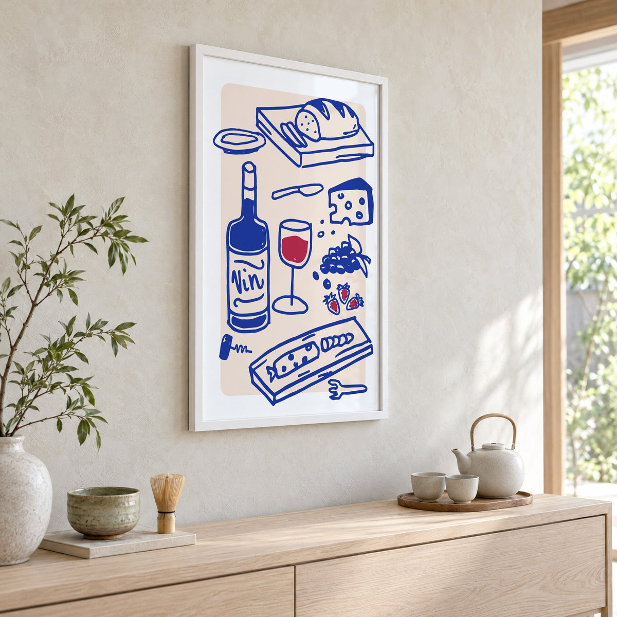 Vin wine and cheese spread print in a white frame above a pale wood console with a matcha tea set