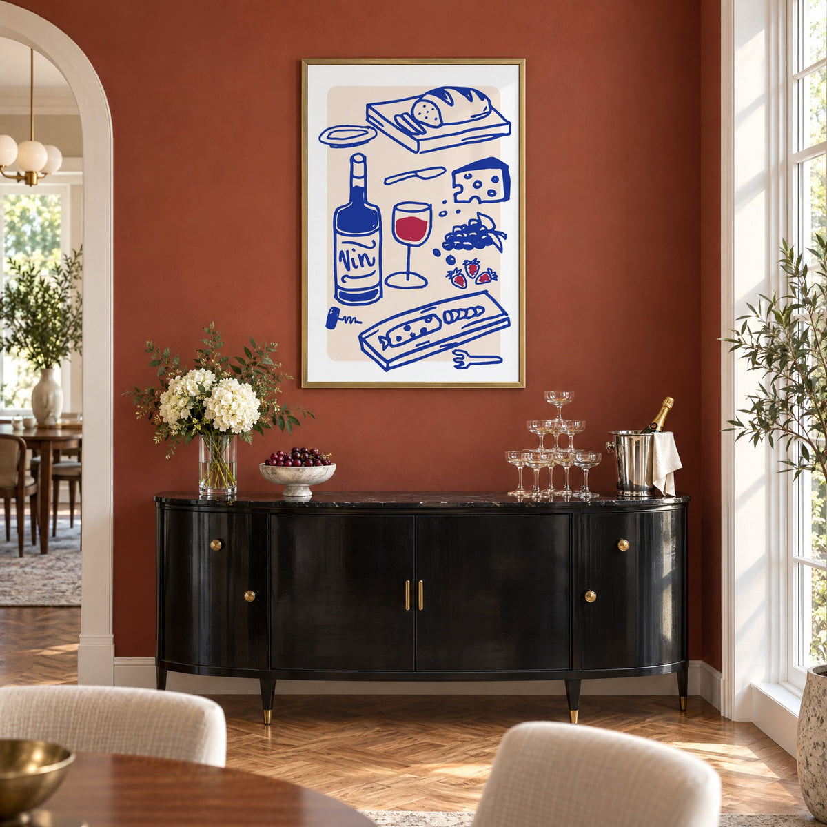 Vin wine and cheese spread print in a brass frame on a terracotta wall above a black buffet with a champagne tower