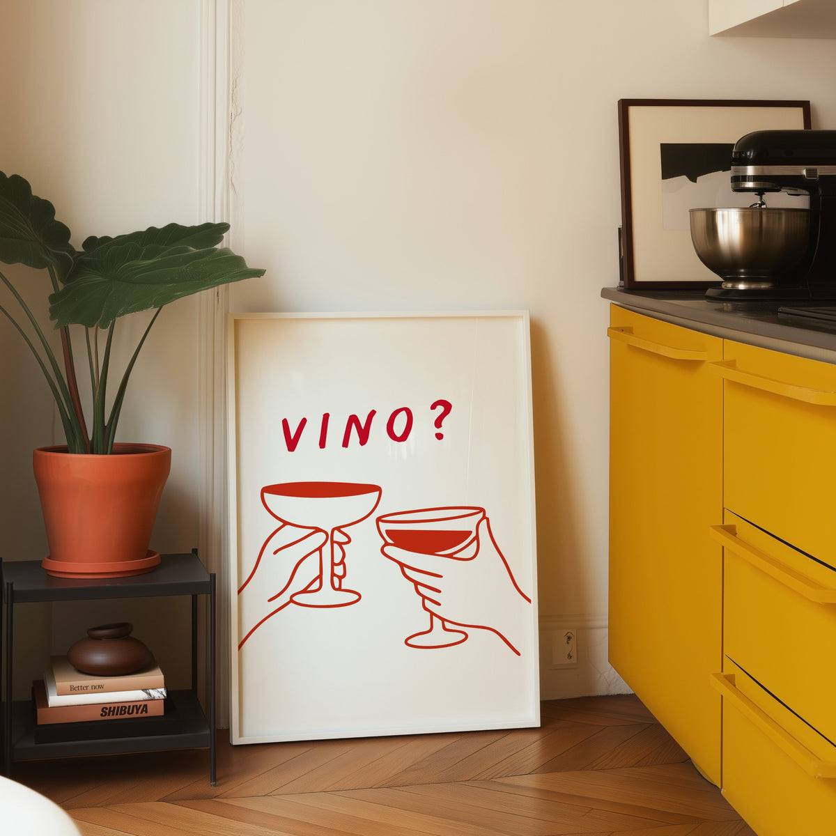 Vino print in a white frame leaning on parquet beside a bright yellow kitchen