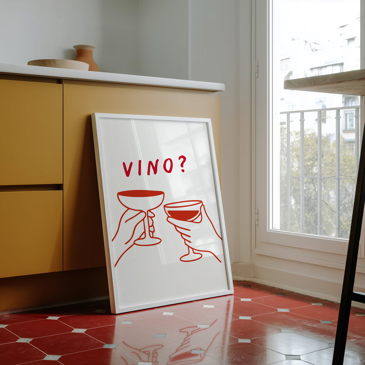 Vino print in a white frame against yellow cabinets on a red tiled floor