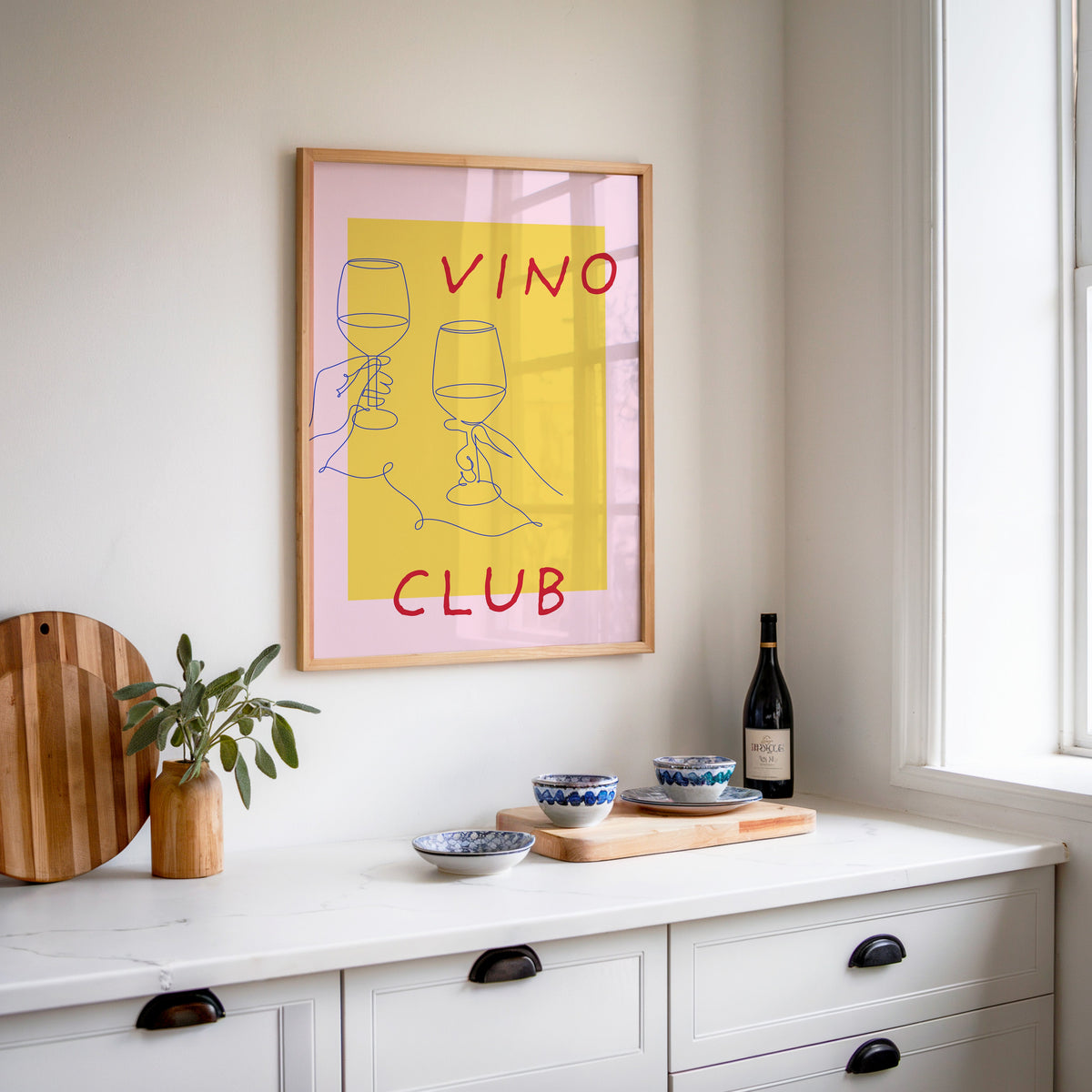 Vino Club print in an oak frame above a white sideboard with a bottle of wine