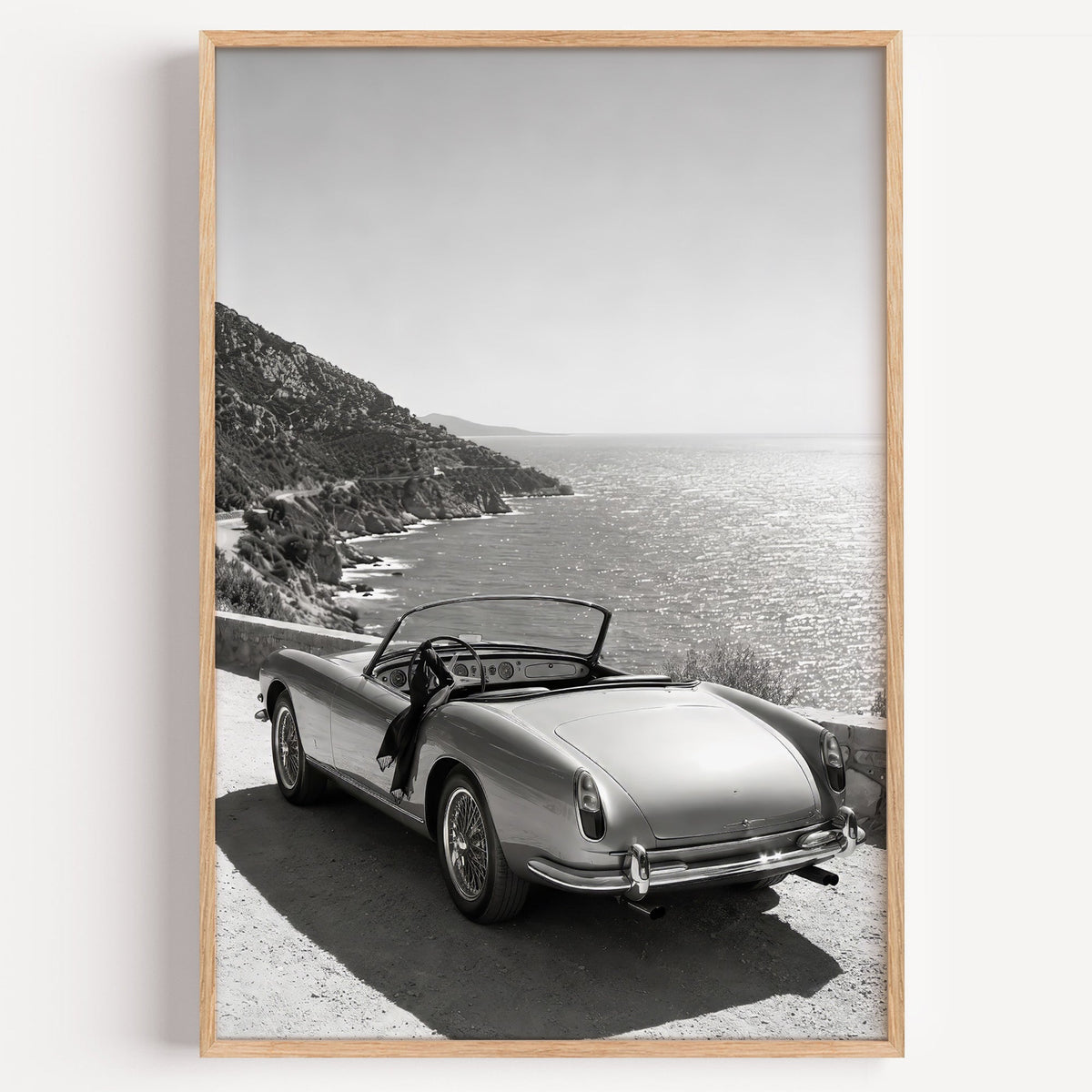 Vintage convertible parked above the sea print in a light oak frame on a plain white wall