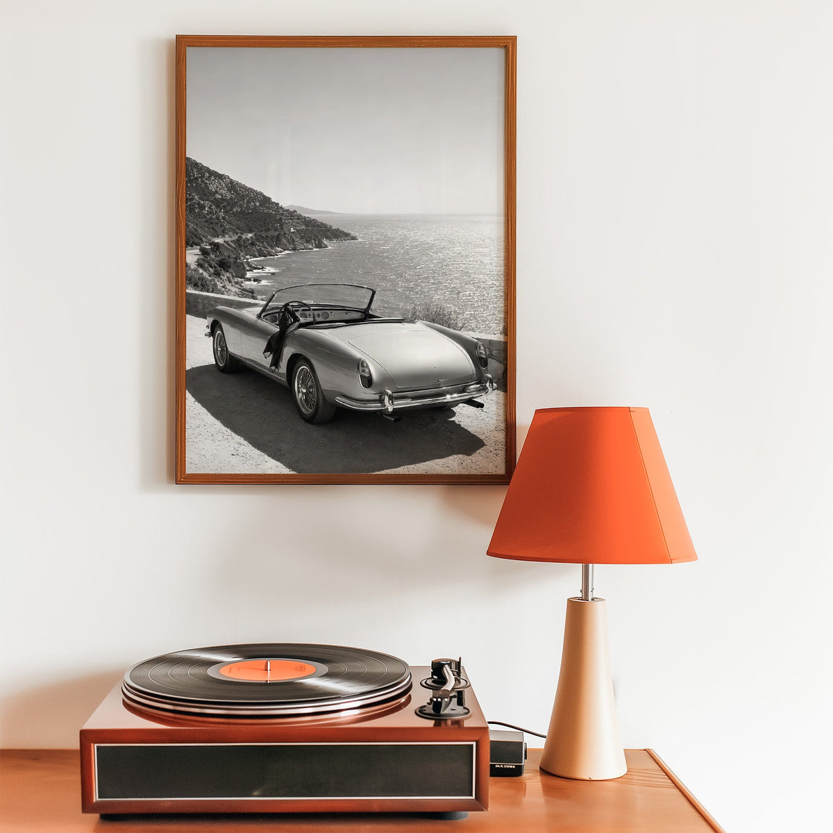 Vintage convertible parked above the sea print in a walnut frame above a record player and orange lamp