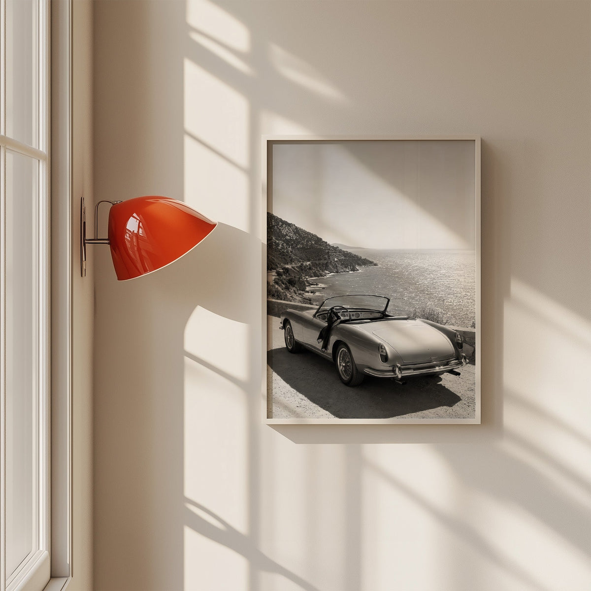 Vintage convertible parked above the sea print in a white frame on a sunlit wall beside a red sconce