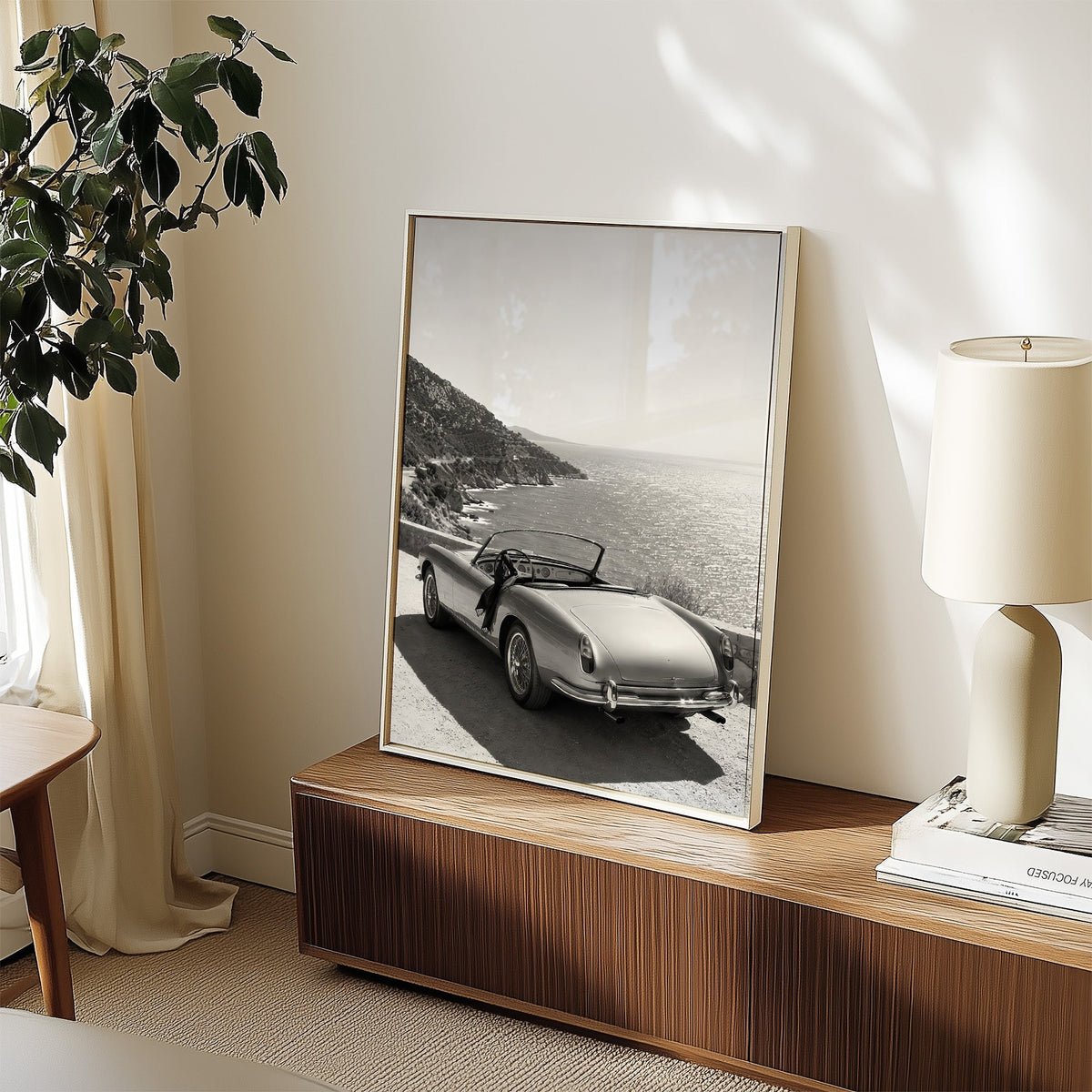 Vintage convertible parked above the sea print in a white frame on a walnut sideboard beside a ceramic lamp