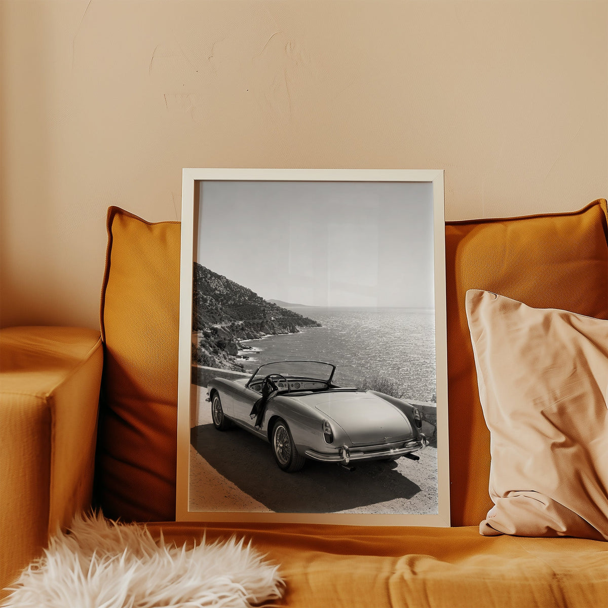 Vintage convertible parked above the sea print in a white frame leaning on a mustard velvet sofa