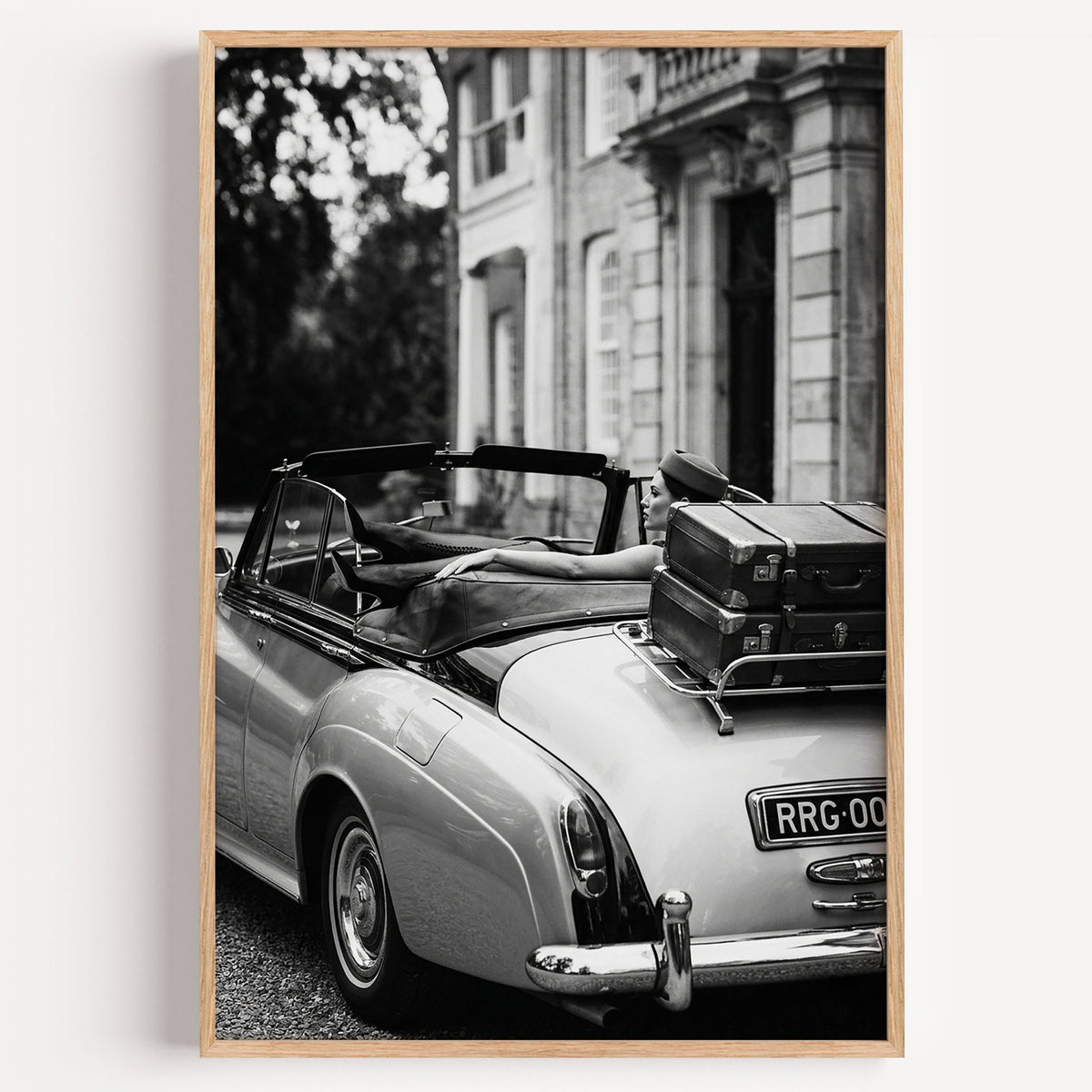 Woman in vintage convertible with leather suitcases print in a light oak frame on a plain white wall