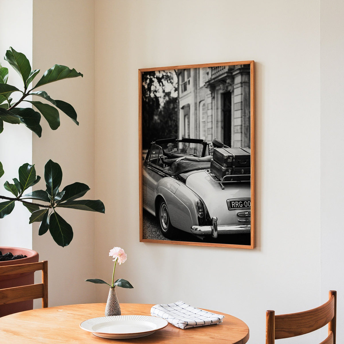 Woman in vintage convertible with leather suitcases print in a teak frame above a round wooden dining table