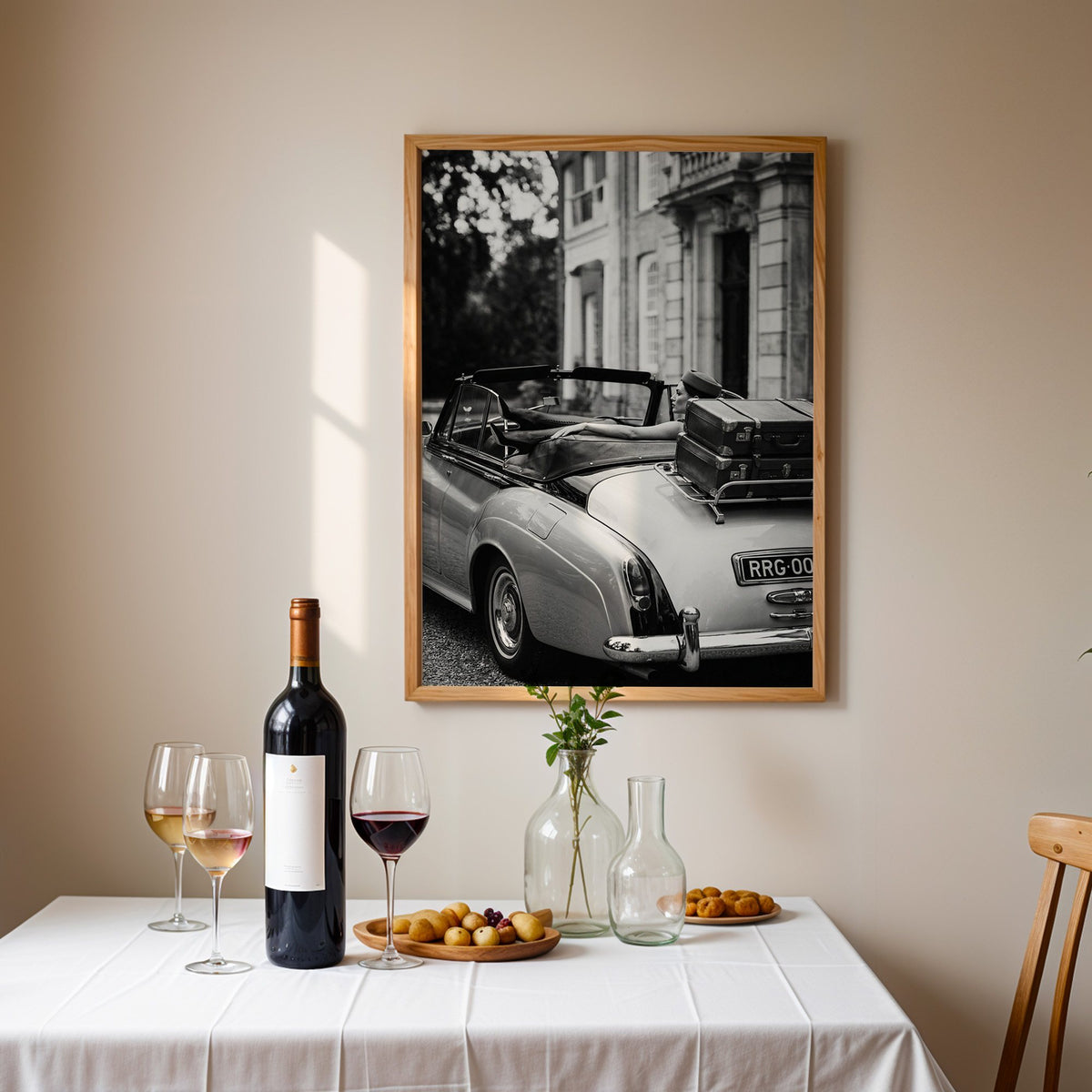 Woman in vintage convertible with leather suitcases print in an oak frame above a table set with red wine and glasses