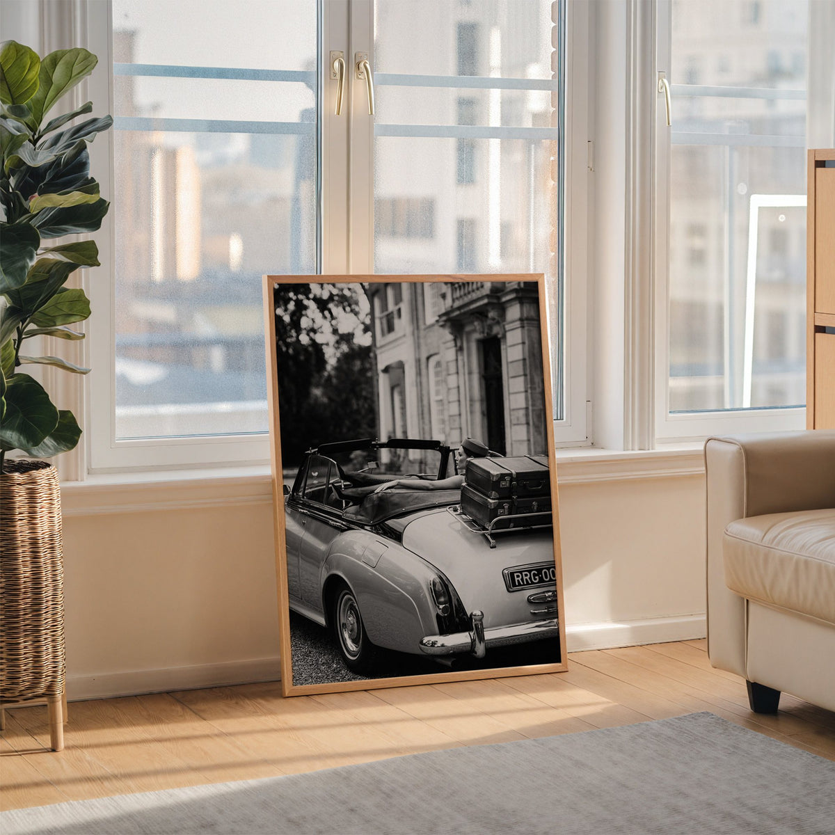 Woman in vintage convertible with leather suitcases print in an oak frame leaning on the floor beside a fiddle leaf fig