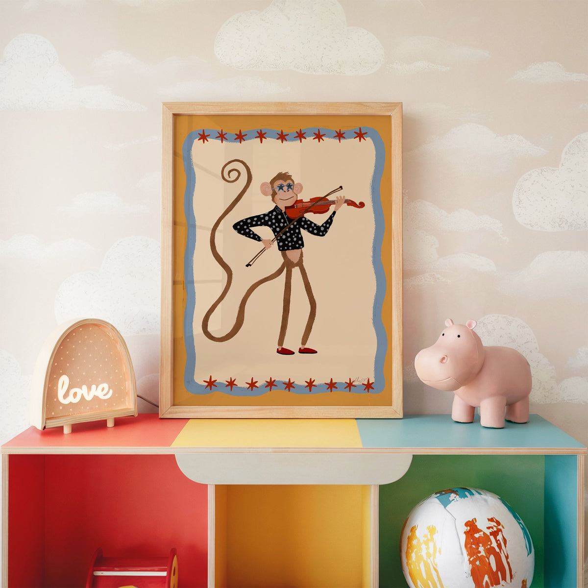 Monkey playing red violin nursery print in an oak frame on a rainbow toy shelf against cloud wallpaper