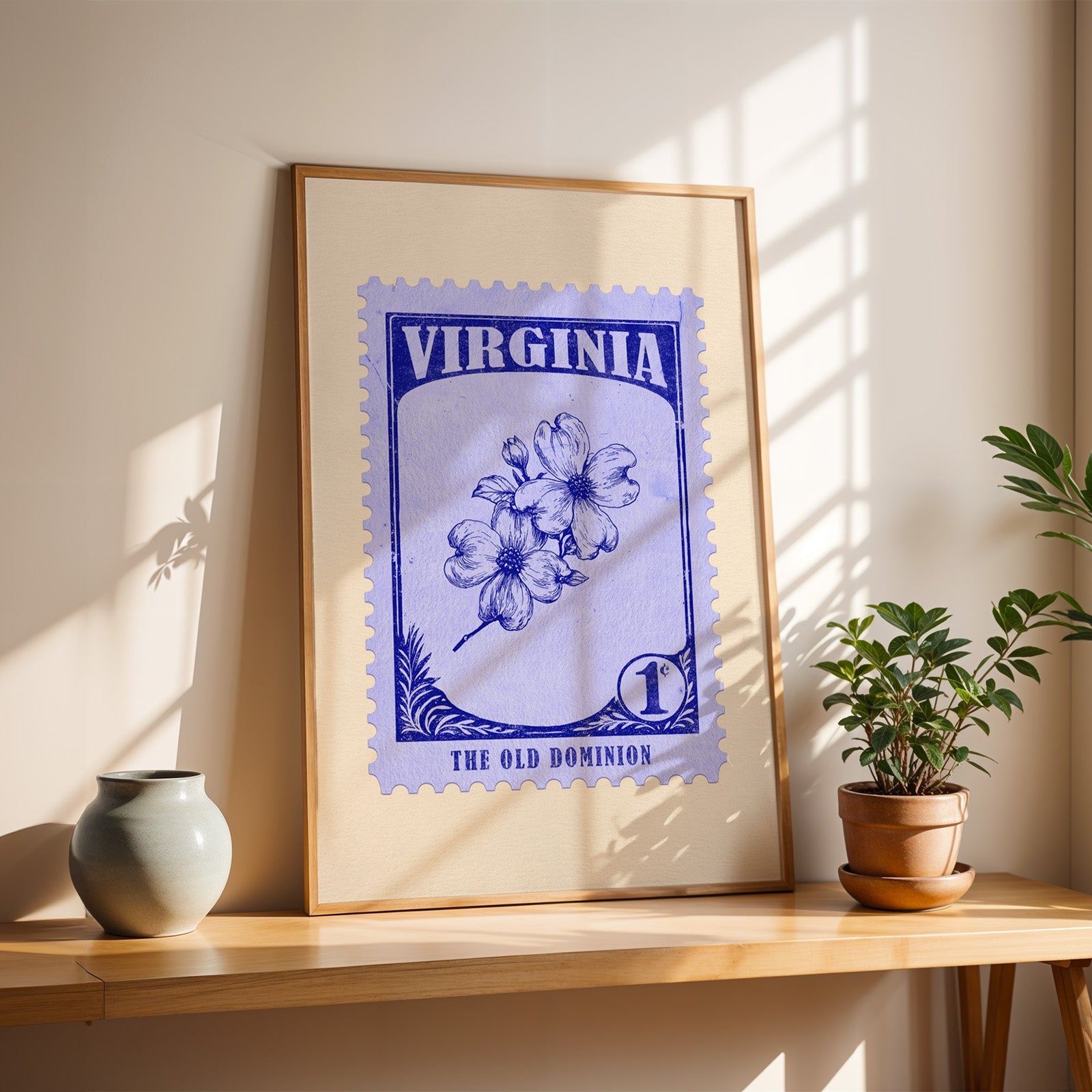 Virginia Dogwood stamp print in a light oak frame leaning on a wooden table beside a stoneware vase