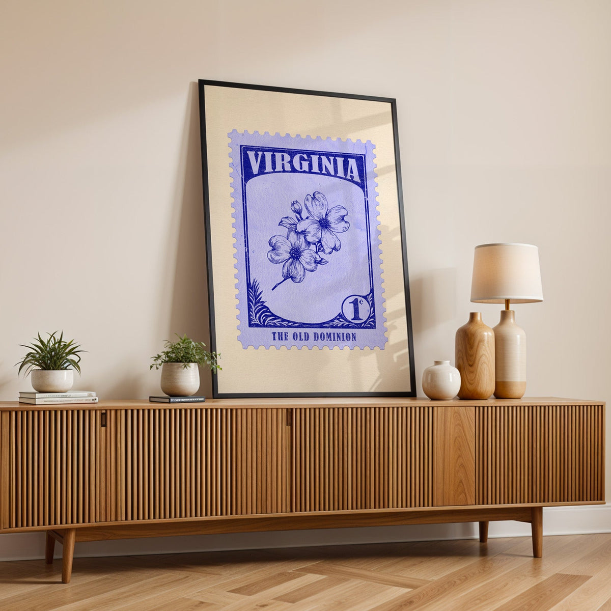 Virginia state flower print in a black frame leaning on a fluted wood credenza with vases and a lamp
