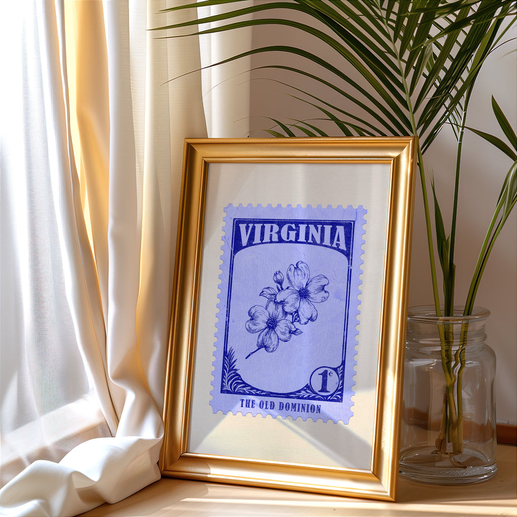 Virginia stamp print in a gold frame leaning by a cream curtain with a palm in a glass jar