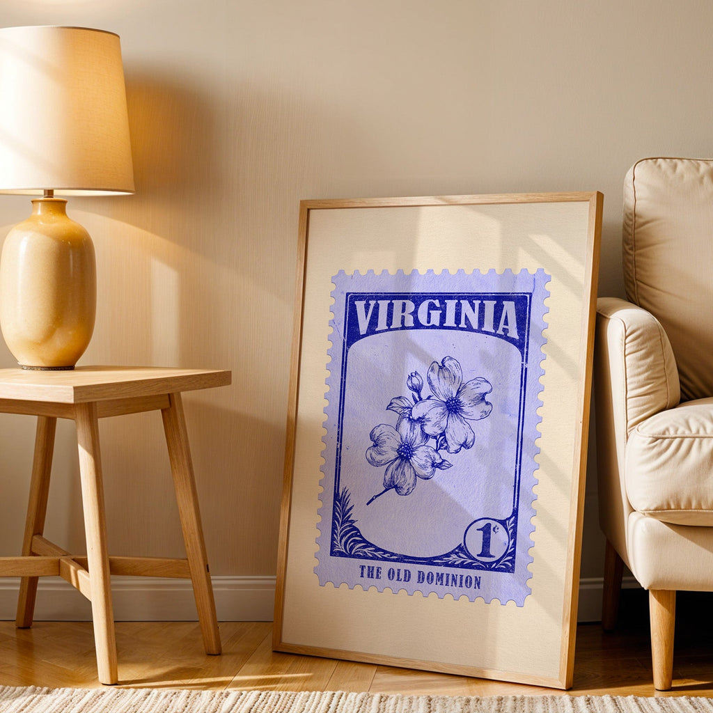 Virginia stamp print in a wood frame resting on the floor beside a beige armchair and a yellow lamp