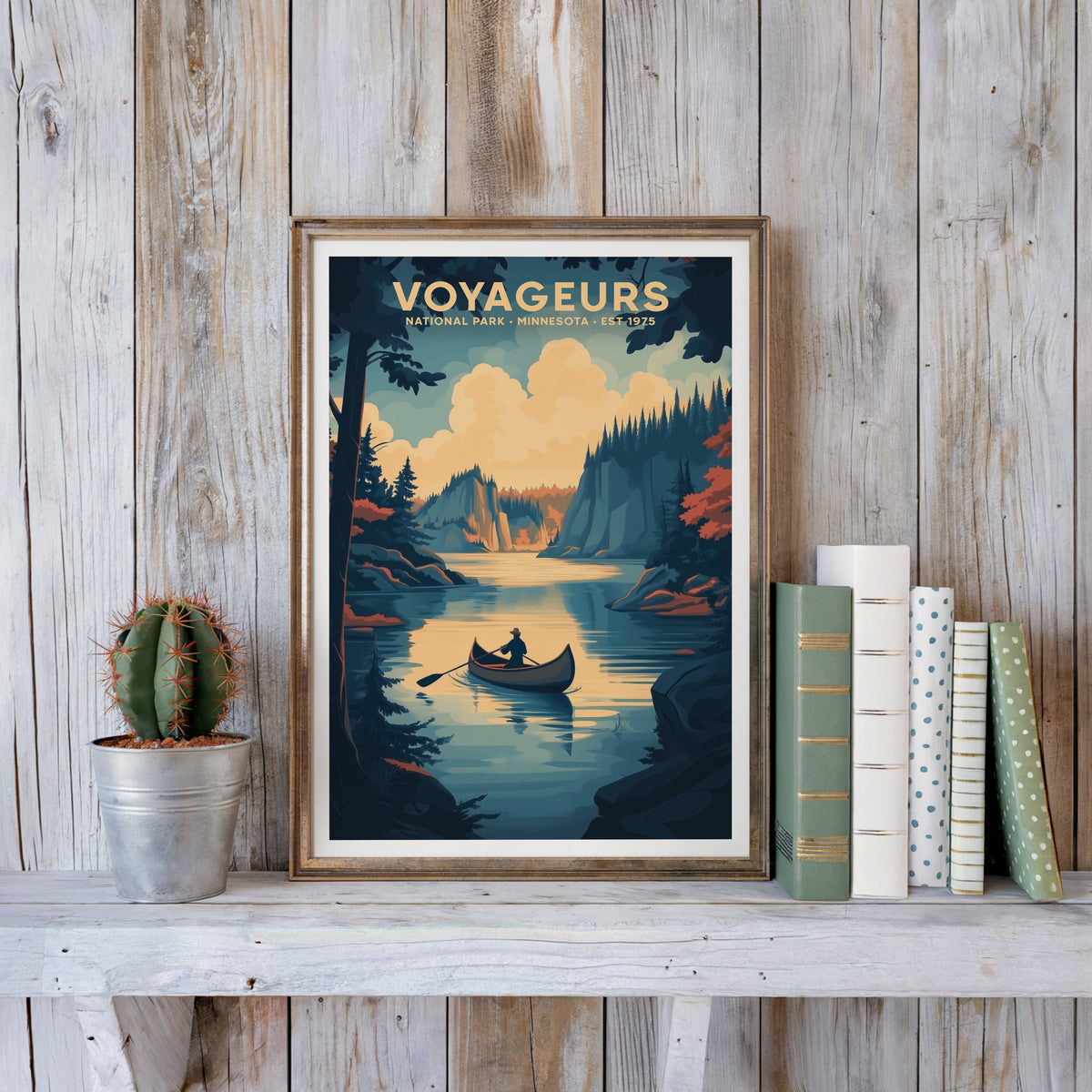 Voyageurs poster in an antique gold frame against whitewashed farmhouse planks beside books and a cactus