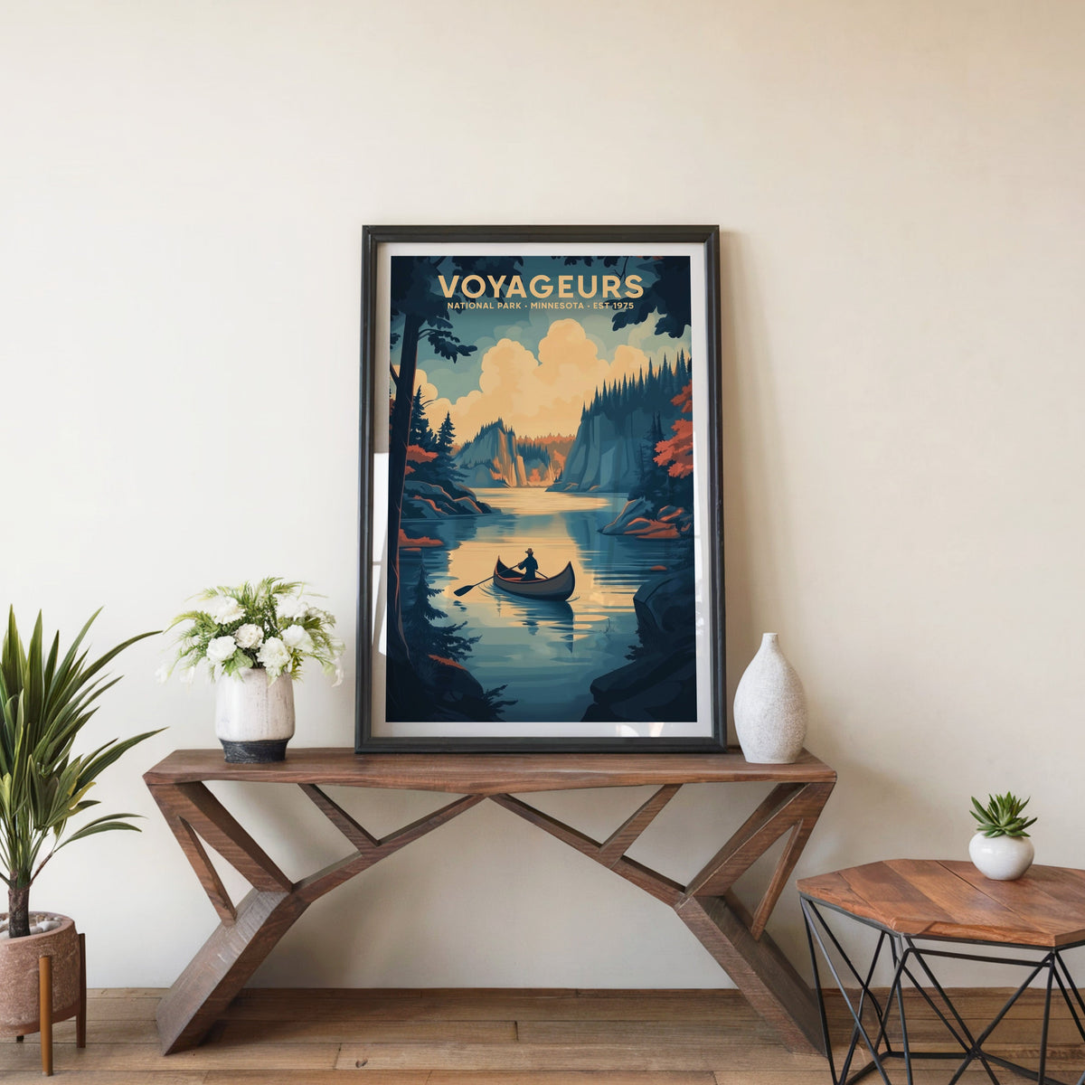 Voyageurs poster in a black frame on an entryway console table beside white flowers and a yucca