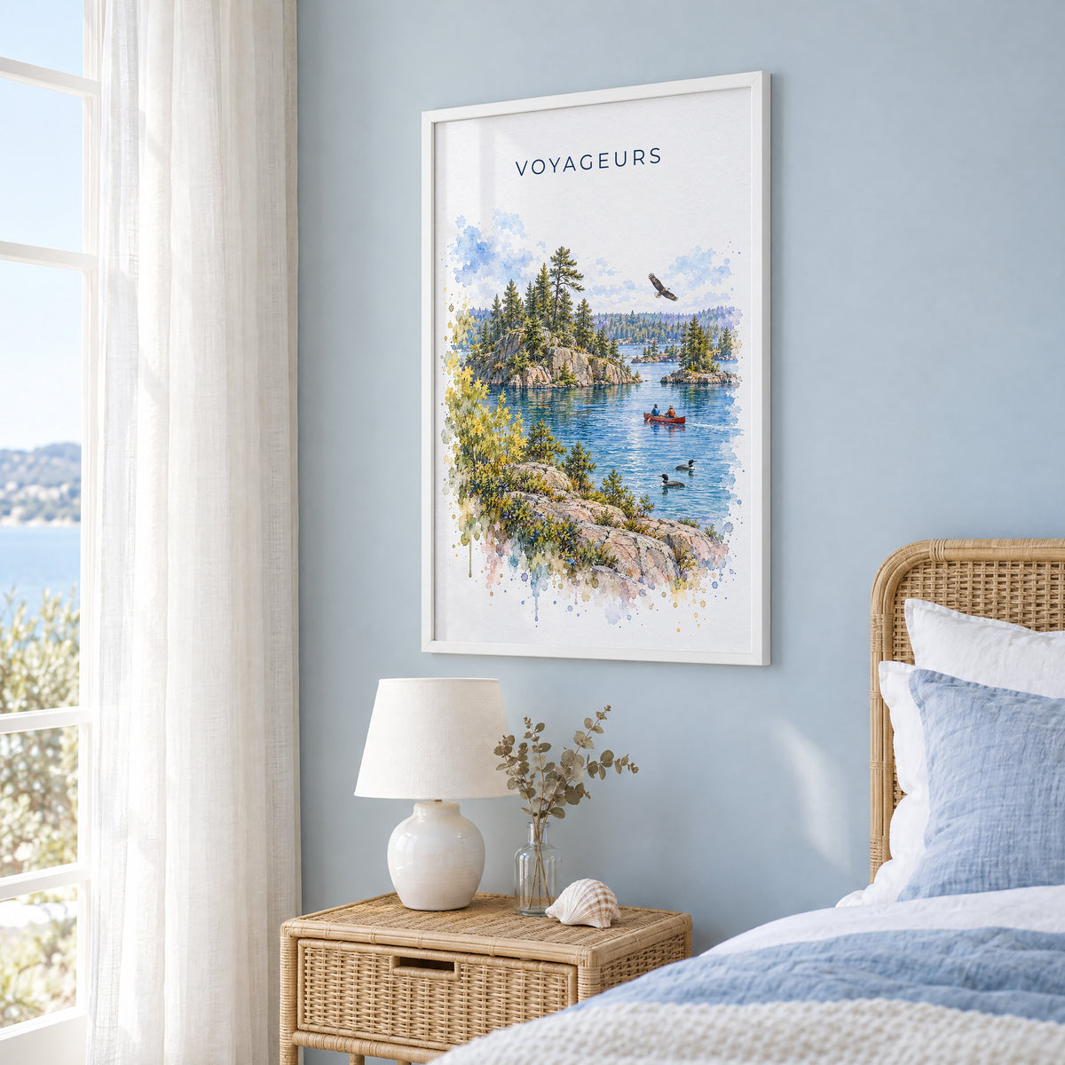 Voyageurs National Park watercolor print in a white frame on a pale blue wall beside a rattan bed in a coastal bedroom