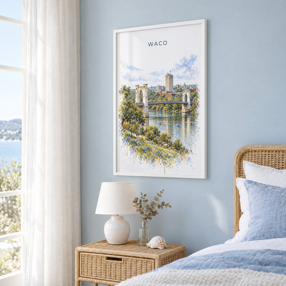 Waco watercolor print in a white frame on a pale blue wall beside a rattan bed in a coastal bedroom