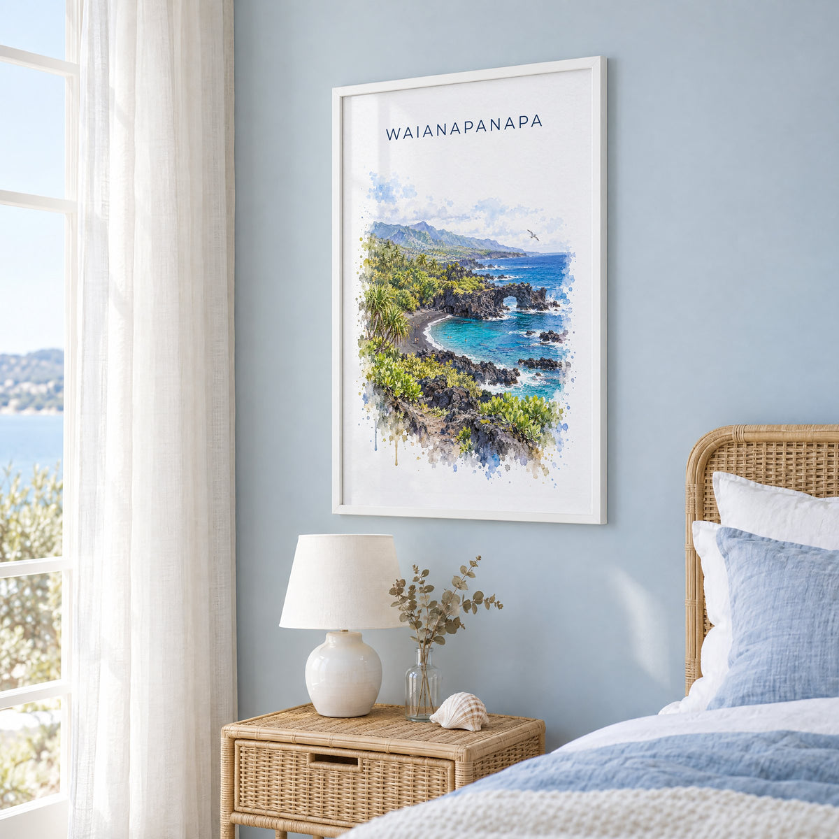 Waianapanapa State Park watercolor print in a white frame on a pale blue wall beside a rattan bed in a coastal bedroom