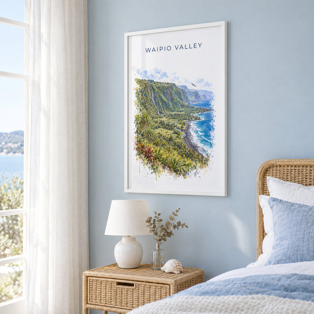 Waipio Valley watercolor print in a white frame on a pale blue wall beside a rattan bed in a coastal bedroom