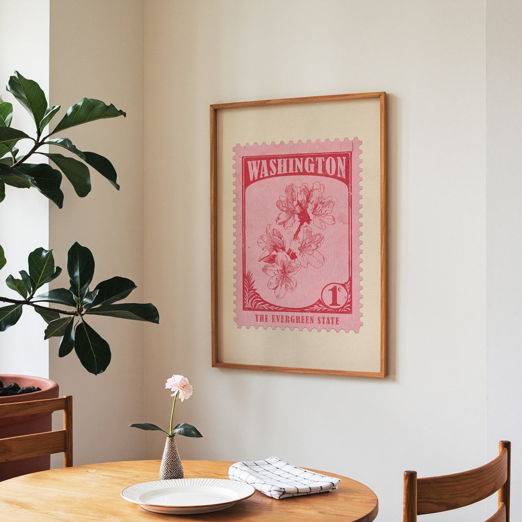 Washington state flower print framed above a round wooden table with a single bloom in a vase and books