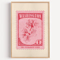 Washington state flower stamp print in crimson on pink, light oak frame on a plain white wall
