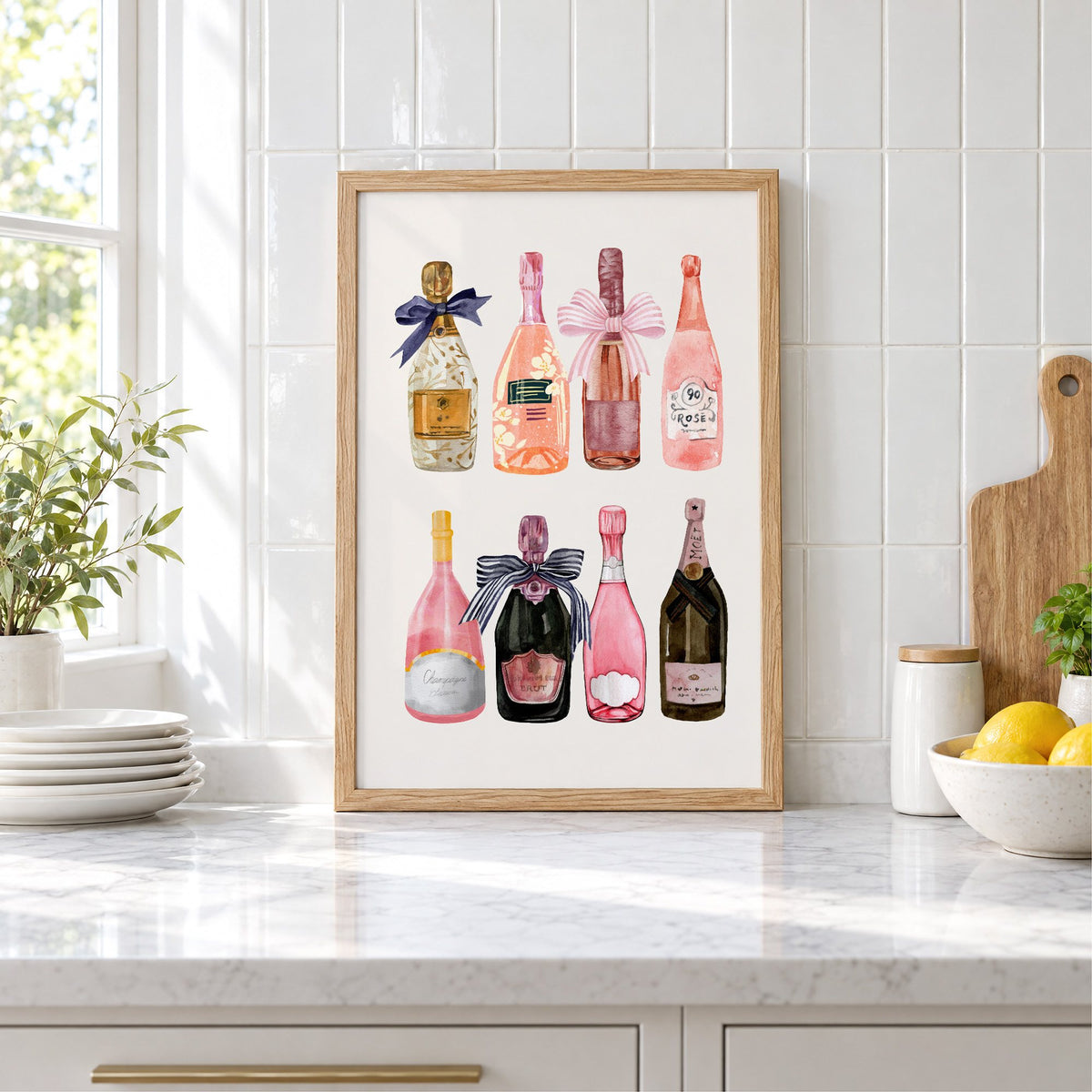 Watercolor champagne bottles print in an oak frame leaning on a marble counter by white tiles and lemons