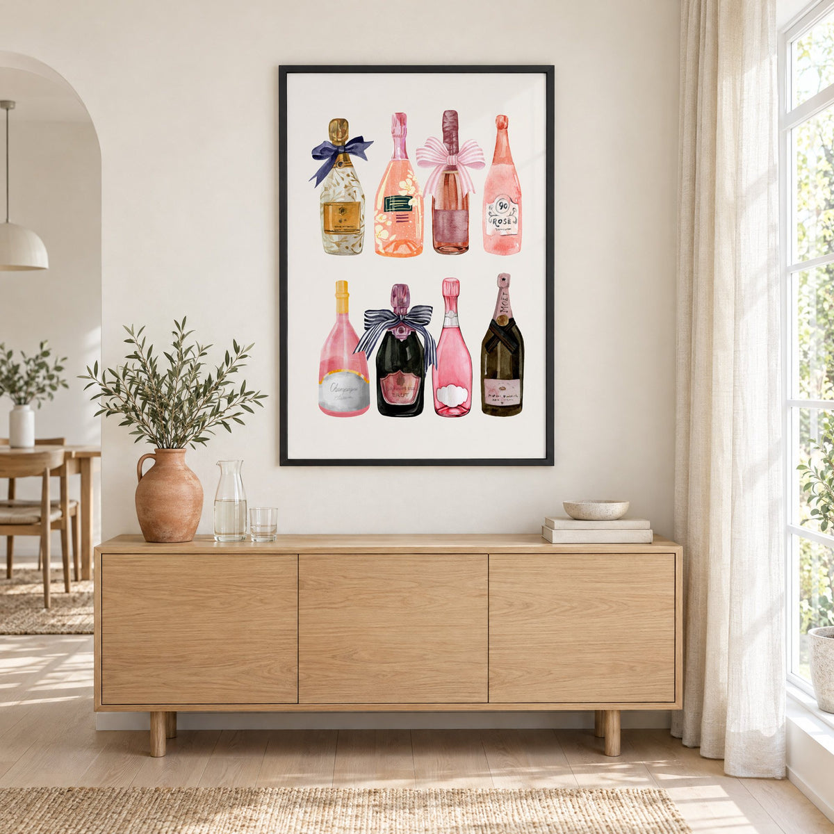 Watercolor champagne bottles print in a black frame above an oak sideboard with a terracotta vase of olive branches