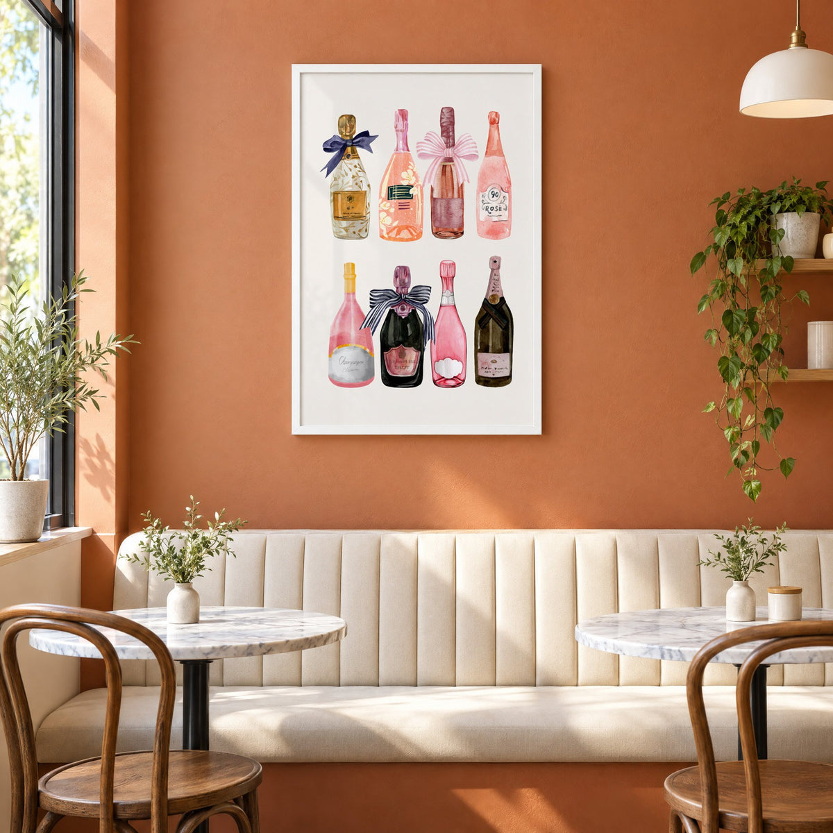 Watercolor champagne bottles print in a white frame above a cream banquette on a terracotta cafe wall