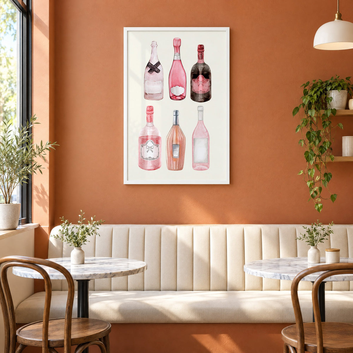 Six pink wine bottles watercolor print in a white frame above a cream banquette on a terracotta cafe wall