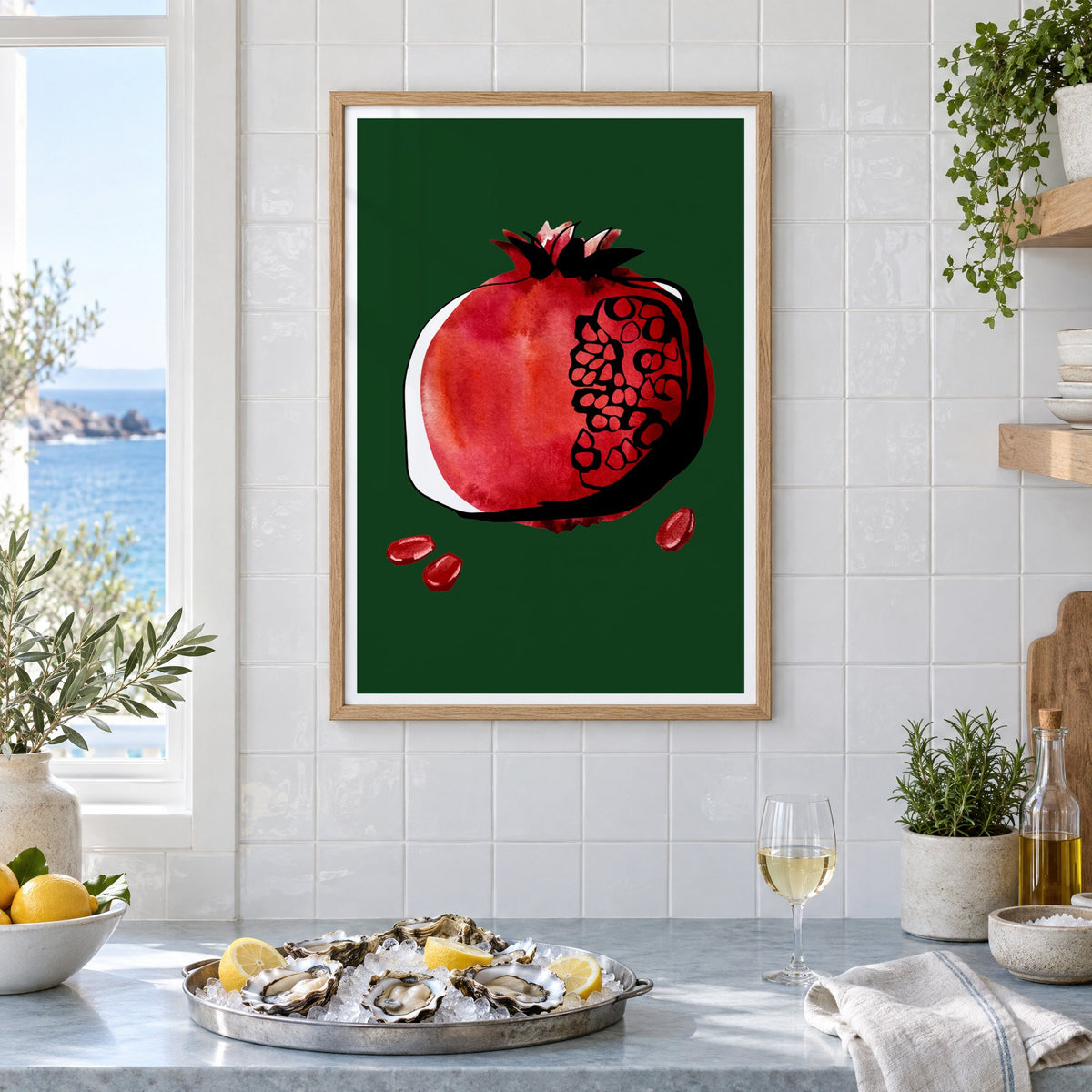 Red watercolor pomegranate on dark green print in an oak frame on white tiles above a marble counter with oysters and lemons by a sea view