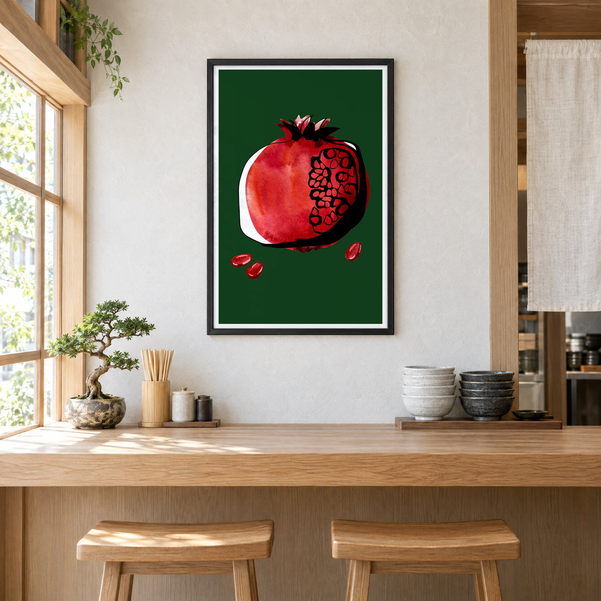 Red watercolor pomegranate on dark green print in a black frame above a light wood ramen counter with stools and stacked bowls
